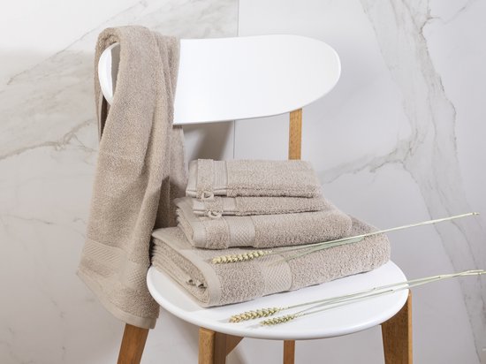 Serviettes beige empilées sur une chaise blanche. Une grande serviette est suspendue à la chaise.