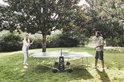 Man en vrouw spelen tafeltennis op een blauw-grijze tafel in een tuin.