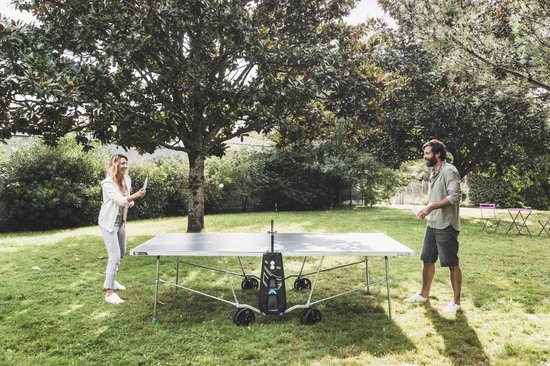 Man en vrouw spelen tafeltennis op een blauw-grijze tafel in een tuin.
