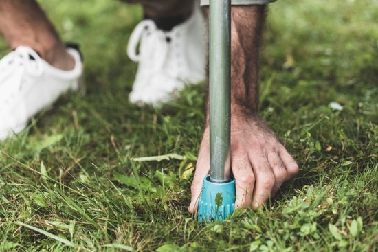 Een hand met witte sneakers plaatst een blauwe, getande voet in gras.