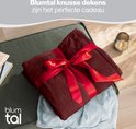 Bordeauxrode fleecedeken opgevouwen en gestrikt met een rood lint, als cadeau.