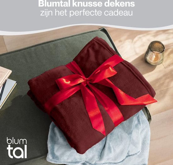 Bordeauxrode fleecedeken opgevouwen en gestrikt met een rood lint, als cadeau.
