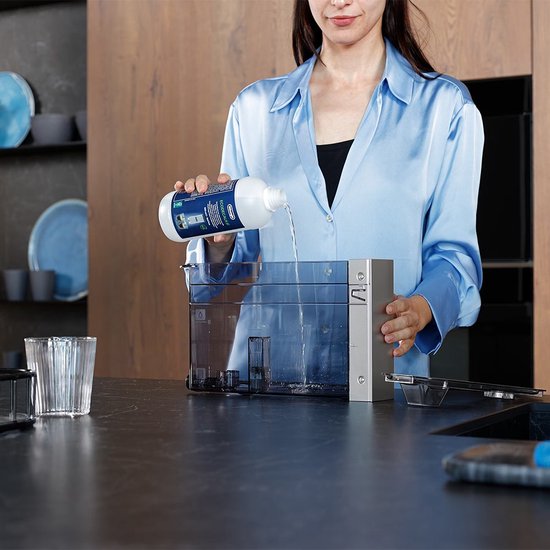 Vrouw in blauw satijnen blouse giet ontkalker in een koffiemachine reservoir.