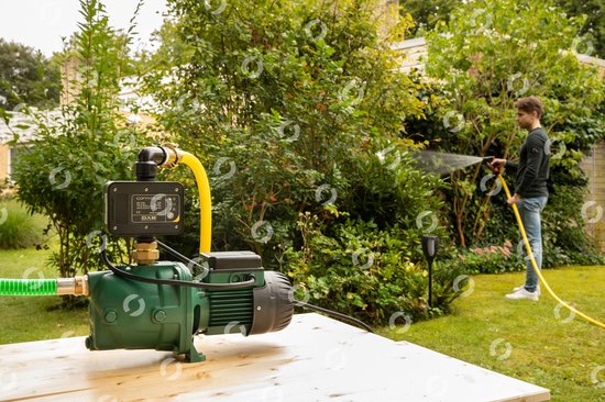 Groene DAB waterpomp met control-d unit, aangesloten op een gele tuinslang. Een man sproeit met de slang in een tuin.