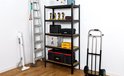 Zwarte metalen stellingkast met 5 houten planken, vol met gereedschap en opbergkoffers.
