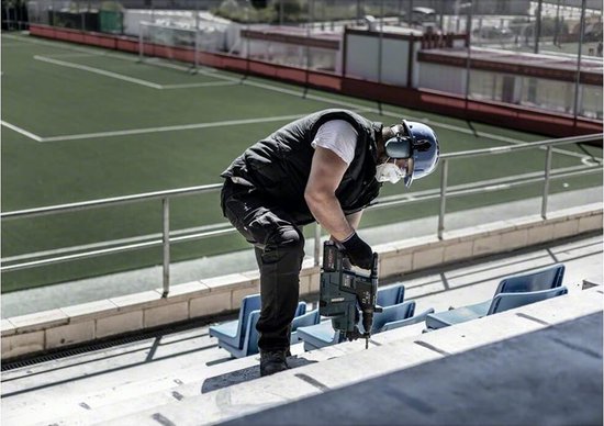 Man met veiligheidsuitrusting gebruikt een boorhamer op een trap.