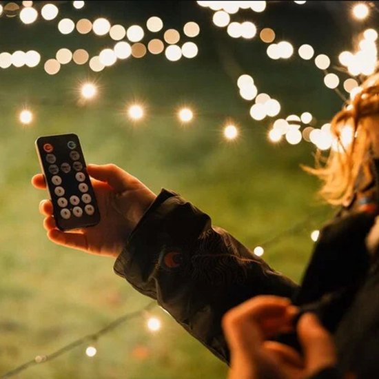 Hand met afstandsbediening, met kerstverlichting op de achtergrond.