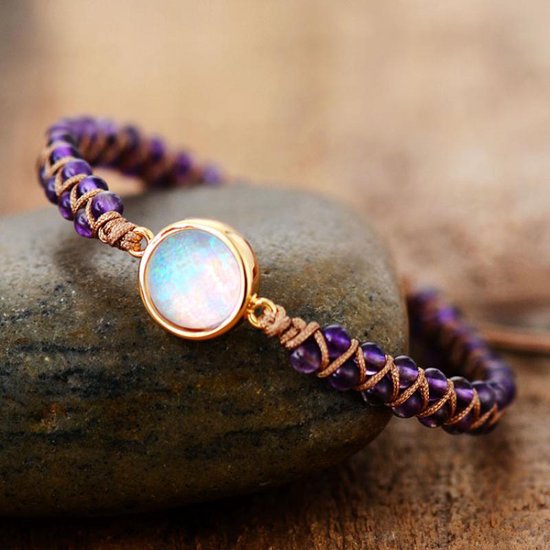 Gevlochten armband met paarse amethist kralen en een ronde, witte Marly Quartz steen, liggend op een steen.