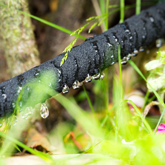 Zwarte druppelslang met waterdruppels die uit de slang vallen, omringd door gras.