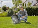 Man reinigt een zwarte robotmaaier met een hogedrukreiniger in een groene tuin.