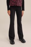Model draagt een zwarte flared legging, gecombineerd met een zwart shirt met ruches en zwarte loafers.