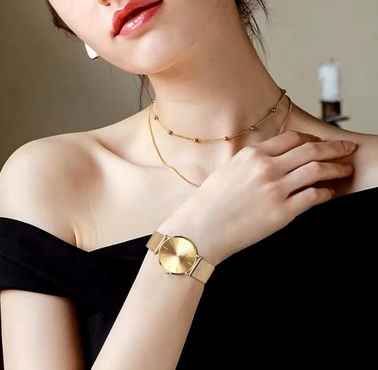 Femme portant une montre Hannah Martin dorée au poignet, robe noire épaules dénudées.