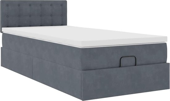 Donkergrijs bed met gestoffeerd hoofdbord, witte matrastopper en opbergruimte.