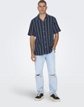 Man in donkerblauw gestreept overhemd en gescheurde lichtblauwe jeans.