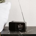 Zwarte Lenco wekkerradio op een marmeren nachtkastje naast een wit kussen.