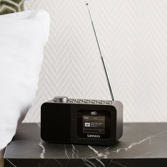 Zwarte Lenco wekkerradio op een marmeren nachtkastje naast een wit kussen.