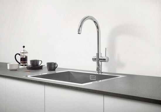 Chroom GROHE keukenkraan boven een metalen gootsteen, met bijpassende mokken en koffiezetter ernaast.