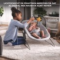 Een meisje speelt met een baby in een grijze schommelstoel op een zacht kleed. De schommelstoel is lichtgewicht en makkelijk te verplaatsen.
