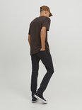Man met bruine t-shirt, zwarte jeans, bruine pet en sneakers, van achteren gezien. Zwart denim.