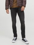 Man draagt een donkerbruine pufferjas, bruine trui en donkergrijze slim fit jeans met witte sneakers.