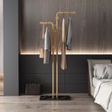 Gouden kapstok met marmeren voet, met kleding en tas eraan. In een slaapkamer.