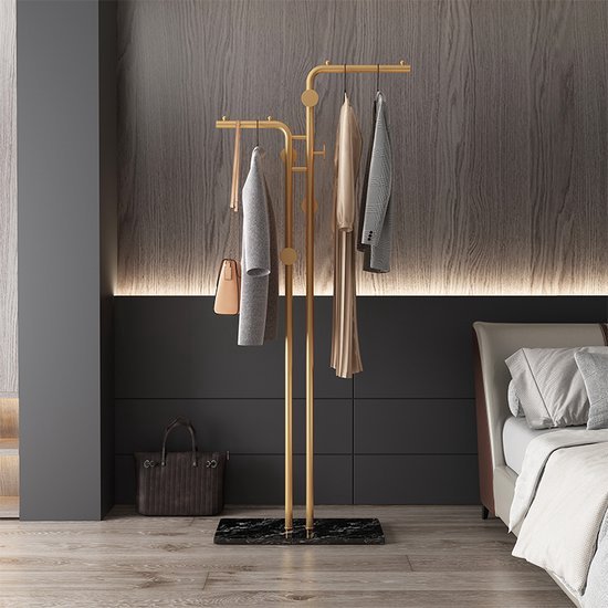 Gouden kapstok met marmeren voet, met kleding en tas eraan. In een slaapkamer.