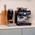 Zwarte koffiemolen en zilverkleurige espressomachine op een aanrecht, met gekleurde kopjes bovenop de machine.