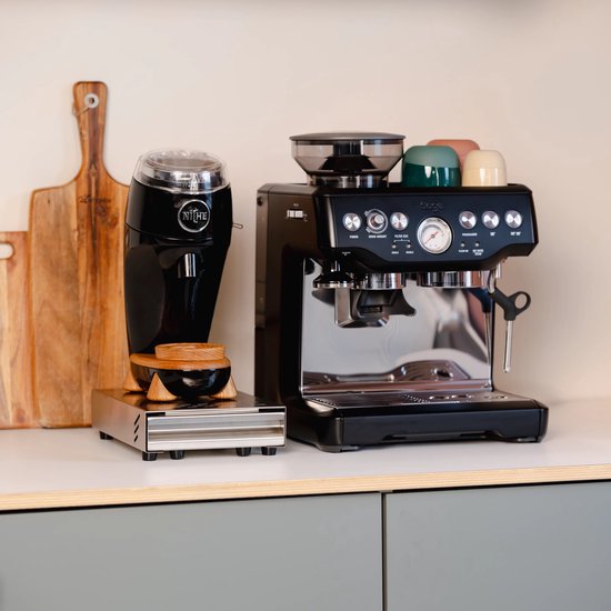 Zwarte koffiemolen en zilverkleurige espressomachine op een aanrecht, met gekleurde kopjes bovenop de machine.