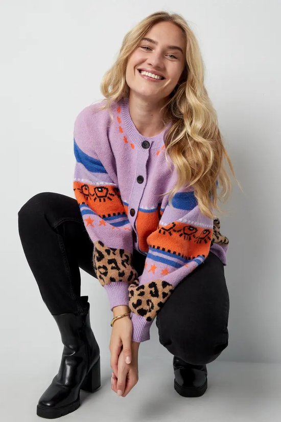 Vrouw met blonde haren, draagt paars vest met luipaardprint, hartjes en blauwe strepen.