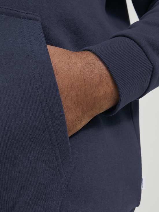 Hand van een man in de zak van een donkerblauwe hoodie. Jack & Jones logo label zichtbaar.