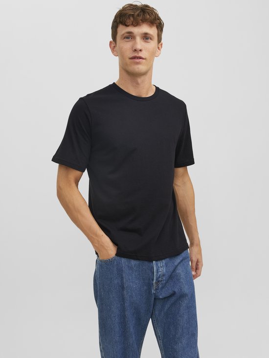 Man met de handen in de zakken van een spijkerbroek, draagt een zwart T-shirt.