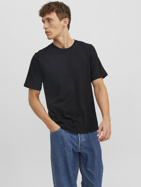 Man met de hand in de zak, draagt een zwart T-shirt en een spijkerbroek.
