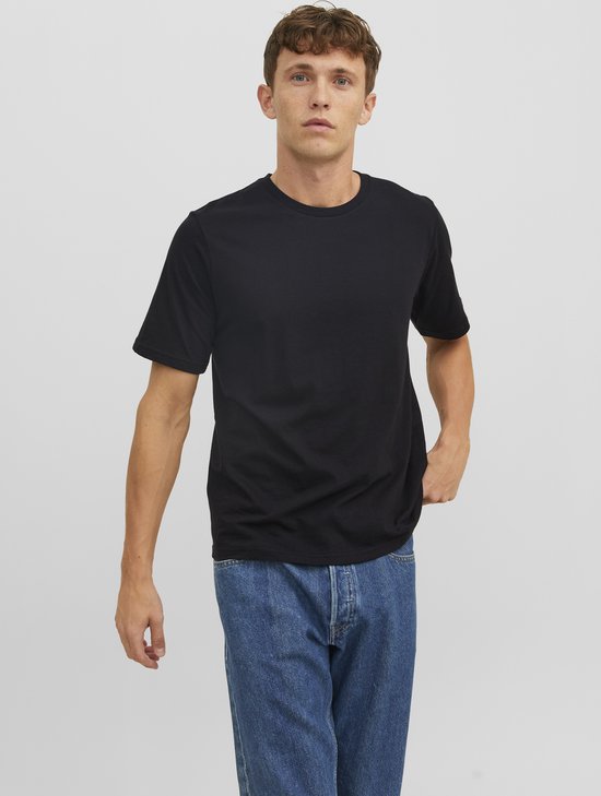 Man met de hand in de zak, draagt een zwart T-shirt en een spijkerbroek.