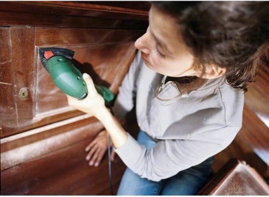 Vrouw schuurt houten kastdeur met een groene Bosch schuurmachine.