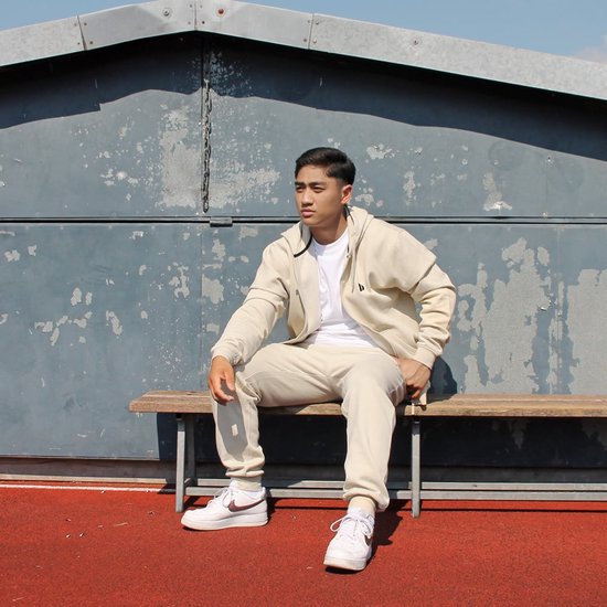 Jongeman in beige trainingspak, zittend op een houten bankje.