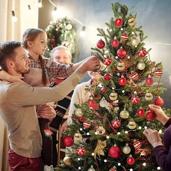Een familie versiert een kerstboom met rode en gouden kerstballen, waaronder ballen met rode strepen en sneeuwvlokken.