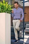 Man in een gestreept blauw overhemd en lichtbeige chino, staand buiten.