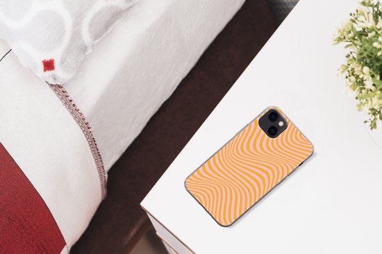Coque pour iPhone 13 mini à motif ondulé orange et rose sur une table de chevet.