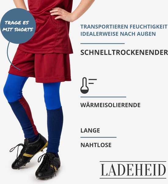 Kind draagt een bordeauxrood sportshirt, rode/blauwe sokken en zwarte voetbalschoenen. De blauwe thermolegging valt tot de knie.