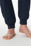 Detail van de enkels en voeten van een man in een donkerblauwe pyjamabroek.