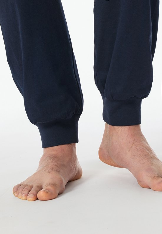 Detail van de enkels en voeten van een man in een donkerblauwe pyjamabroek.