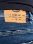 Detail van de bruine leren patch op blauwe jeans met merknaam 'Petrol Industries'.
