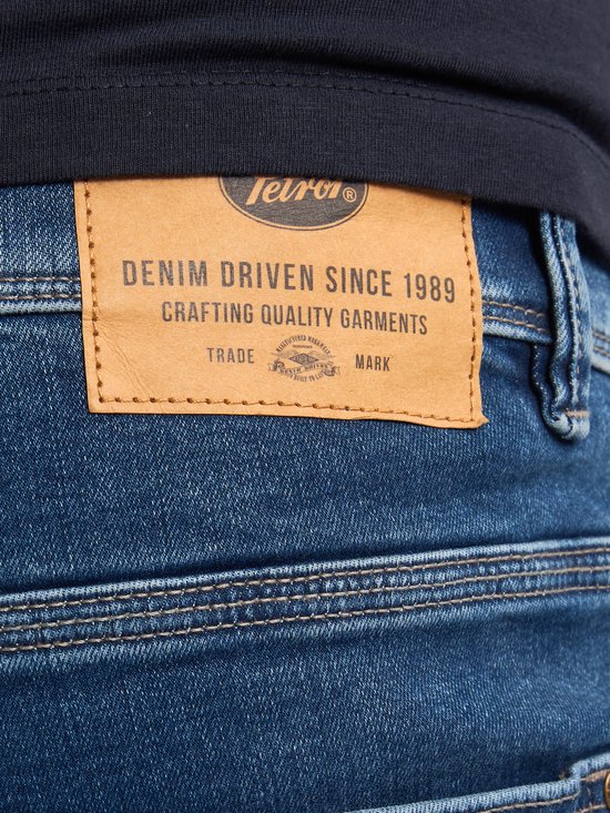 Detail van de bruine leren patch op blauwe jeans met merknaam 'Petrol Industries'.