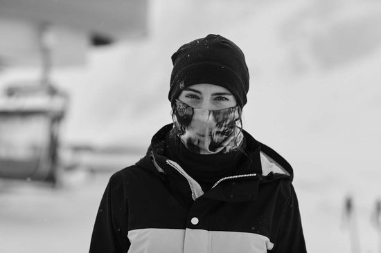 Vrouw met skibril en muts die een nekwarmer als gezichtsmasker draagt met abstracte print.