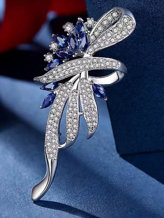 Zilverkleurige broche met blauwe en witte kristallen in een sierlijk bloem- en lintmotief.