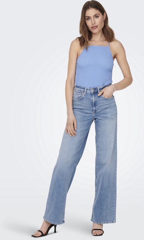 Model in een lichtblauwe, wijde spijkerbroek met hoge taille, blauw topje en sandalen.
