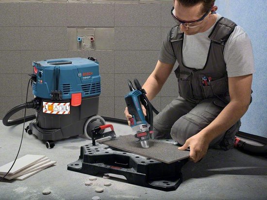 Man gebruikt een Bosch tool met stofzuiger naast betegelde muur.