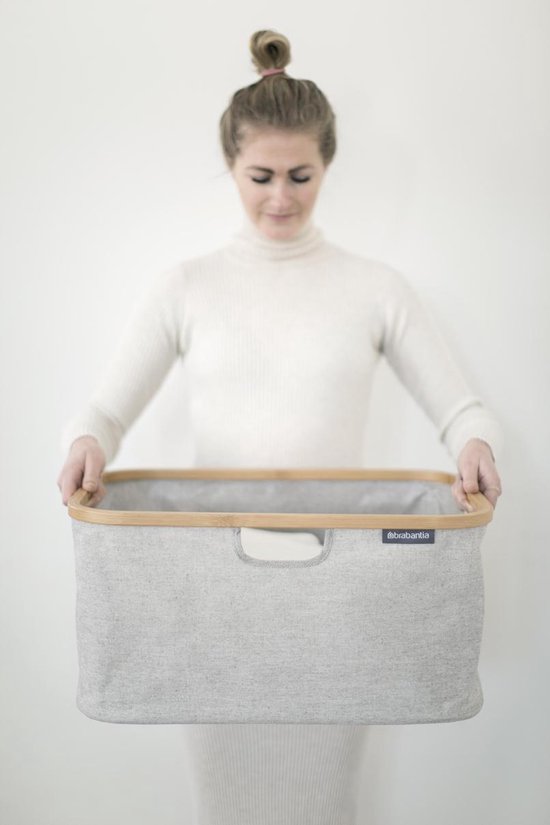 Vrouw met witte coltrui, houdt grijze Brabantia wasmand met bamboe frame vast.