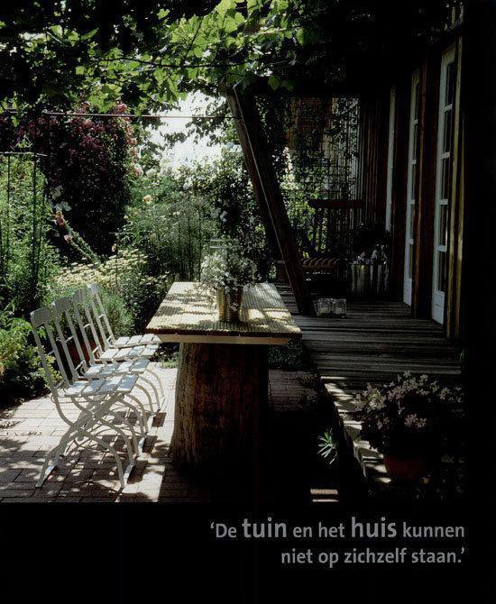 Houten tafel met witte stoelen in een weelderige tuin, met uitzicht op een houten vlonder.