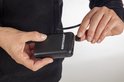 Zwarte powerbank van "BERTSCHAT" die wordt aangesloten op een snoer van een hoodie.
